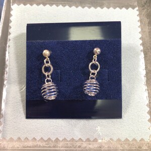 Puede incluir: Un par de pendientes de plata con un cristal azul encerrado en una jaula de alambre. Los pendientes cuelgan de un bucle de plata.