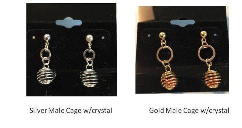 Puede incluir: Dos pares de pendientes con un dise&ntilde;o de jaula. Los pendientes de la izquierda son de plata con un cristal transparente en la jaula. Los pendientes de la derecha son de oro con un cristal rojo en la jaula. Los pendientes est&aacute;n etiquetados como "Silver Male Cage w/crystal" y "Gold Male Cage w/crystal".