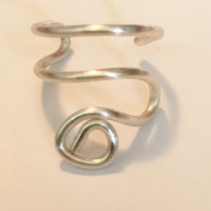 May include: A silver-colored ear cuff with a spiral design. The ear cuff wraps around the ear in a continuous, flowing shape. The metal has a polished finish, reflecting light.