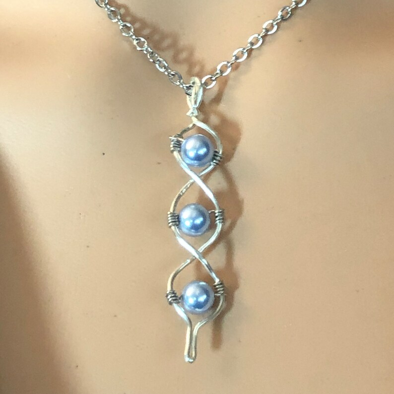 K&ouml;nnte beinhalten: Eine silberne Halskette mit einem Anh&auml;nger, der drei hellblaue Perlen in einem gedrehten Drahtdesign zeigt.