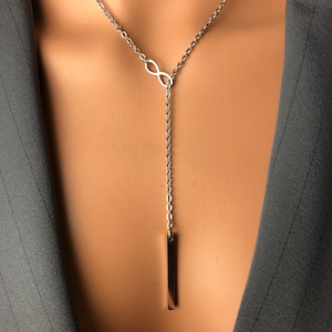 May include: A silver infinity symbol pendant necklace with a long, thin silver bar hanging from it.