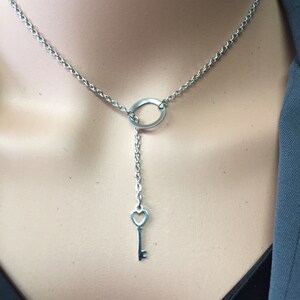 May include: A silver necklace with a circle pendant and a key charm with a heart-shaped hole. The necklace is on a mannequin.