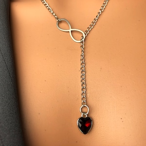 May include: A silver necklace with an infinity symbol and a dangling heart charm with a red gemstone.
