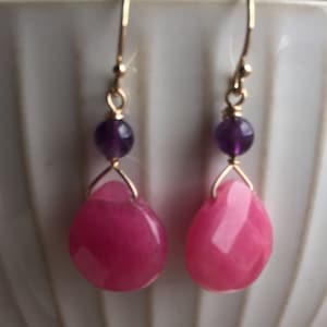 May include: A pair of dangle earrings with pink and purple gemstone beads. The earrings are made with gold-toned metal.