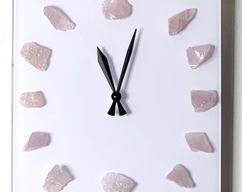 May include: A white square clock with black hands and pink rose quartz crystals around the face.
