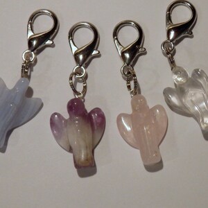 May include: Four angel-shaped crystal charms with silver lobster clasps. The charms are made of clear quartz, rose quartz, amethyst, and blue lace agate.
