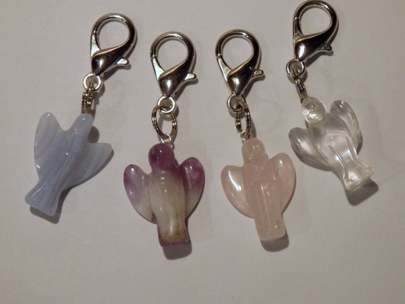 May include: Four angel-shaped crystal charms with silver lobster clasps. The charms are made of clear quartz, rose quartz, amethyst, and blue lace agate.