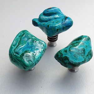 May include: Three bottle stoppers made of green and blue malachite stone. Each stopper has a silver metal base.