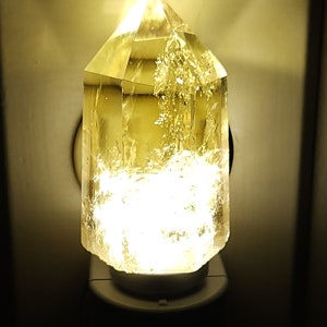 May include: A clear crystal night light shaped like a pyramid with a warm white light shining through it.