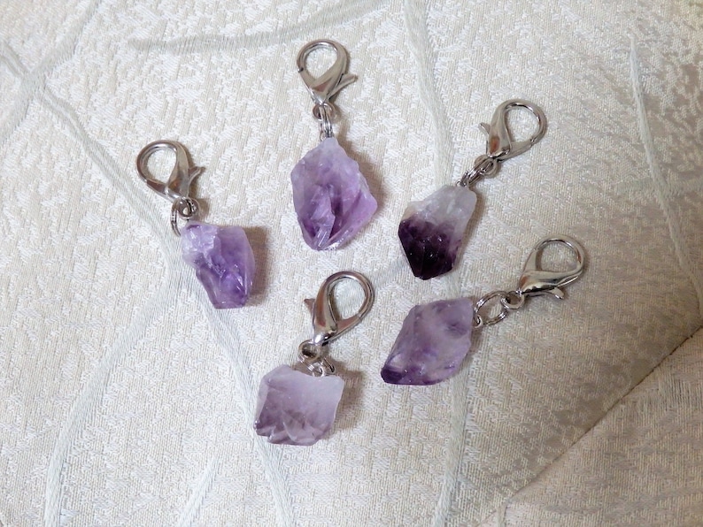 May include: Five amethyst crystal charms with silver lobster clasps. The amethyst crystals are various shapes and sizes.