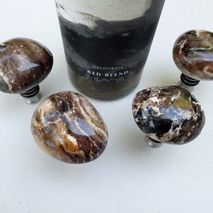 May include: Four brown and white agate stone bottle stoppers with silver metal bases. The stoppers are shaped like rounded stones.
