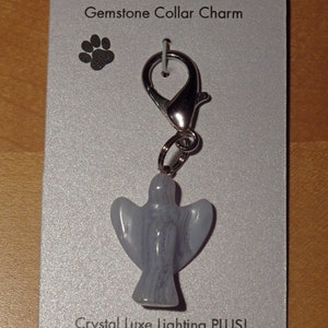 May include: A silver charm with a blue gemstone angel pendant, attached to a silver clasp. The charm is labeled "Kitty Cat Crystals Gemstone Collar Charm" and "Crystal Luxe Lighting PLUS! CrystalLuxeLighting.etsy.com".