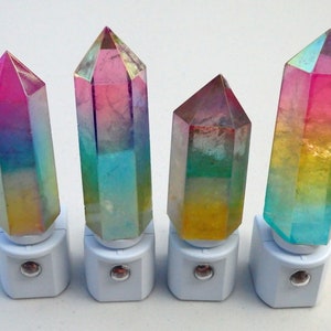 May include: Four decorative night lights with crystal-shaped tops. The crystals have a gradient of colors, including pink, blue, yellow, and green. Each crystal is mounted on a white base with a small, round light.