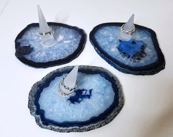 May include: Three blue agate ring holders with white cone-shaped ring stands. Each holder features a unique blue and white agate pattern.