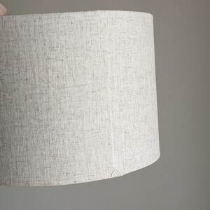 hand holding handmade Calacatta Gold Flax fabric lamp shade showing the back seam with triangle stitch detail
