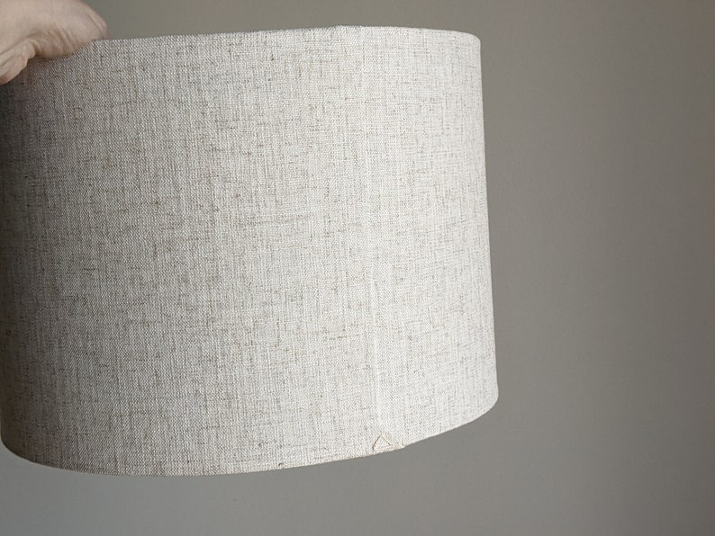 hand holding handmade Calacatta Gold Flax fabric lamp shade showing the back seam with triangle stitch detail