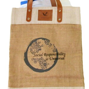 Puede incluir: Una bolsa de mano marr&oacute;n y beige con ribete blanco. La bolsa tiene un asa de cuero marr&oacute;n y un logotipo en la parte delantera. La bolsa tiene un dise&ntilde;o en la parte delantera que dice "Social Responsibility is Universal".
