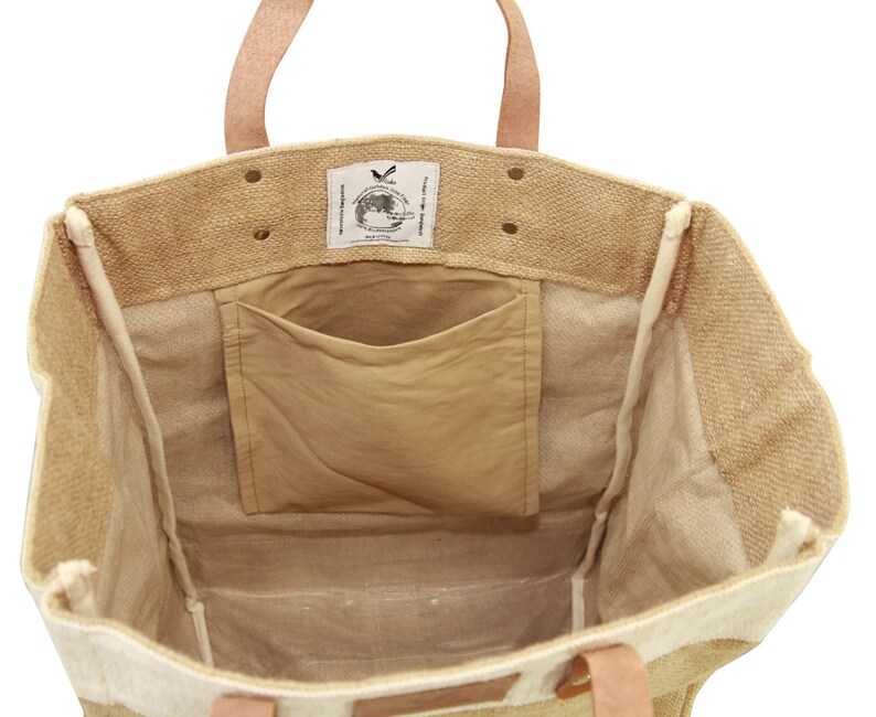 Puede incluir: Una bolsa de tote de yute marr&oacute;n con un forro blanco y un peque&ntilde;o bolsillo interior. La bolsa tiene asas de cuero y una etiqueta con el texto "Made in India" y un gr&aacute;fico de globo terr&aacute;queo.