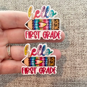 May include: Two colorful stickers with a rainbow pencil and the text "hello first grade".