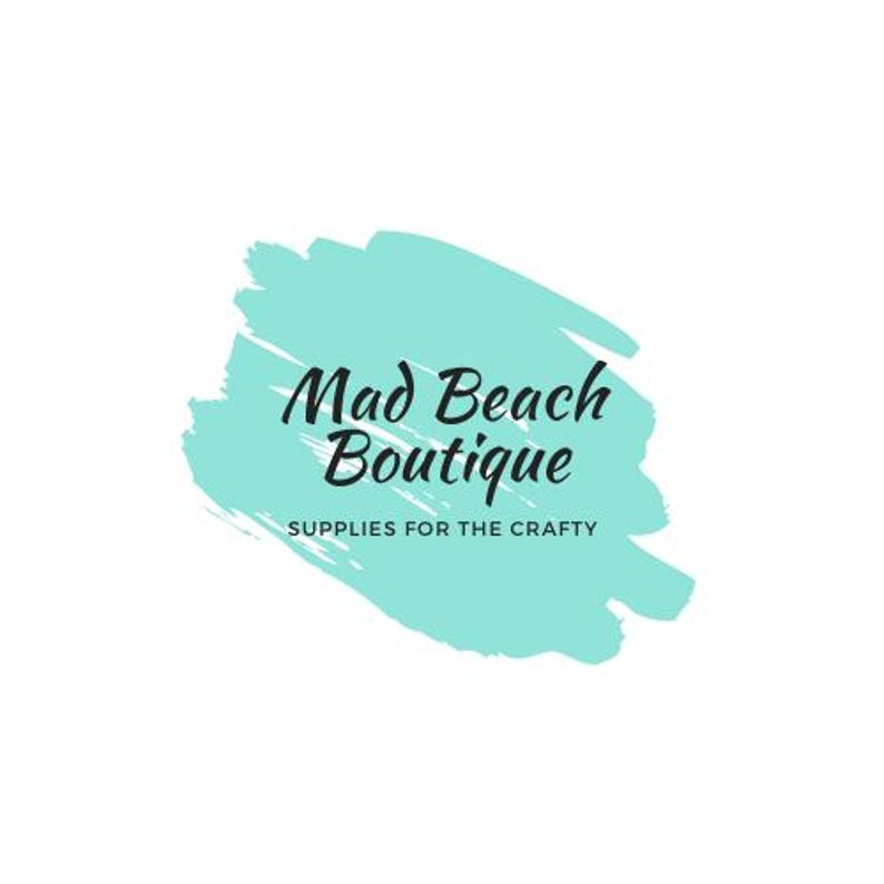 Peut inclure: Le logo Mad Beach Boutique pr&eacute;sente un texte en noir sur une forme de coup de pinceau turquoise. En dessous du nom de la boutique, le texte indique &laquo; SUPPLIES FOR THE CRAFTY &raquo; dans une police plus petite, le tout sur fond blanc.