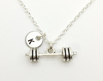 May include: Silver necklace with a barbell charm and a small round charm with the letter K.
