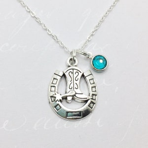 May include: Silver necklace with a horseshoe charm featuring a cowboy boot and a small turquoise blue gemstone.