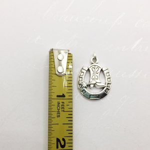 May include: Silver charm with a horseshoe design and a cowboy boot inside. The horseshoe has a star and a small circle on each side.