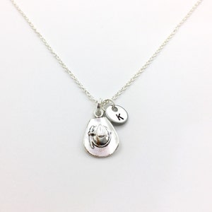 May include: Silver necklace with a charm of a cowboy hat and a small silver disc with the letter K.
