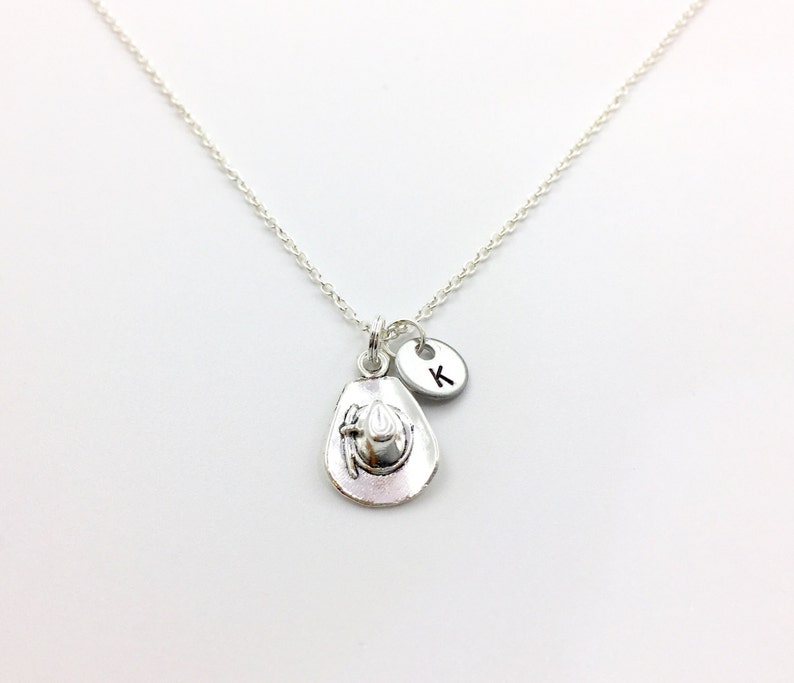 May include: Silver necklace with a charm of a cowboy hat and a small silver disc with the letter K.