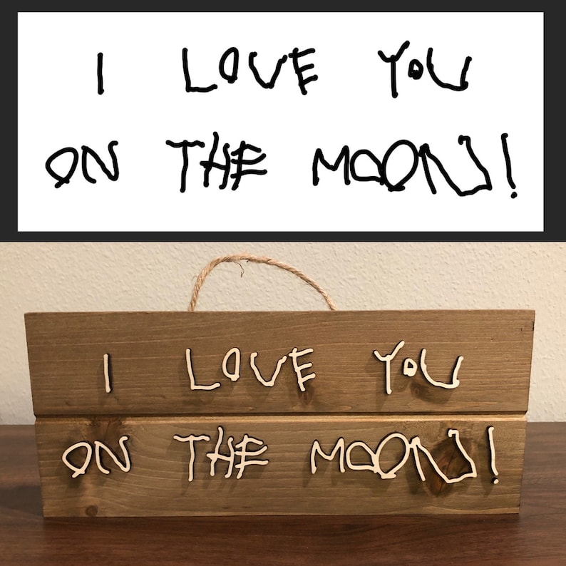 May include: A wooden sign with the words "I love you on the moon!" written in white paint. The sign is hanging from a piece of twine.