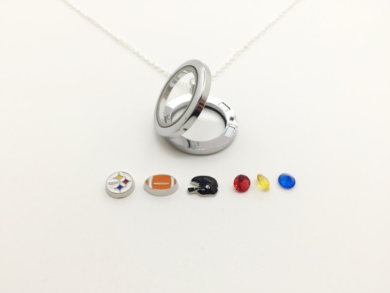 Może przedstawiać: Srebrny naszyjnik z zawieszką, kt&oacute;ra zawiera r&oacute;żne wisiorki, w tym piłkę nożną, logo Steelers, hełm i trzy kamienie szlachetne w kolorze czerwonym, ż&oacute;łtym i niebieskim.