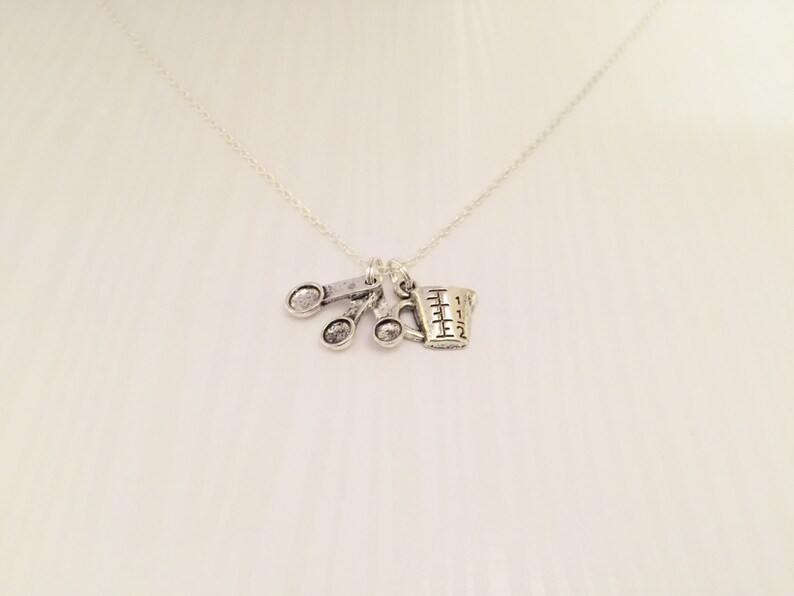 Puede incluir: Collar de plata con un dije de una taza medidora y tres cucharas.