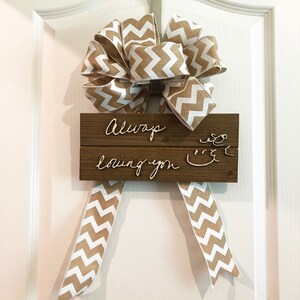 May include: A wooden sign with the text "Always loving you" written in cursive on it. The sign is decorated with a brown and white chevron patterned ribbon bow.
