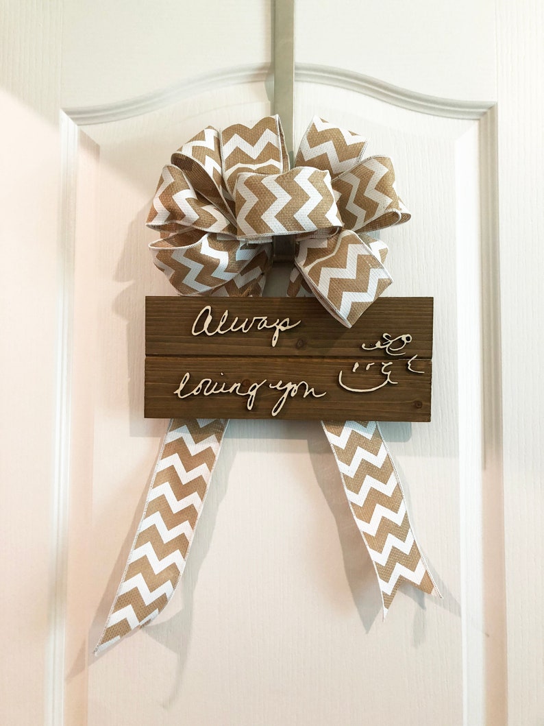 May include: A wooden sign with the text "Always loving you" written in cursive on it. The sign is decorated with a brown and white chevron patterned ribbon bow.