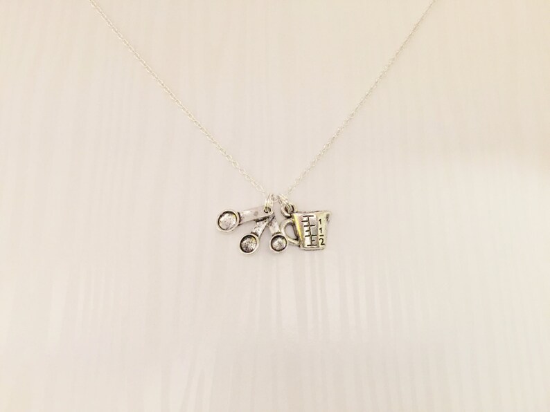 Puede incluir: Collar de plata con un dije de una taza medidora y tres cucharas medidoras. Los dijes est&aacute;n unidos a una cadena de plata.