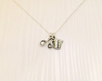 May include: A silver necklace with a charm of a measuring cup and two spoons. The charm is attached to a silver chain.