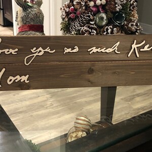 May include: A wooden sign with the text "Love you so much Kenny Mom" written in cursive.