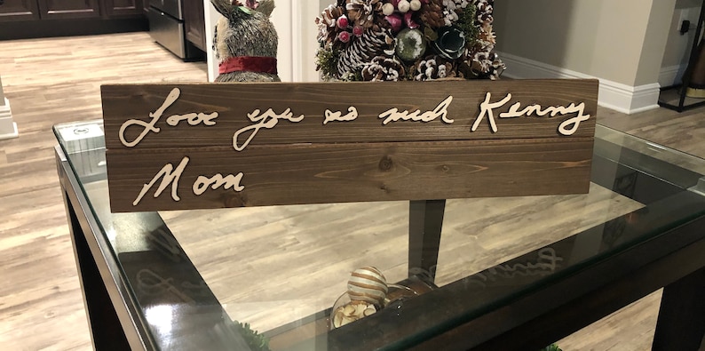 May include: A wooden sign with the text "Love you so much Kenny Mom" written in cursive.