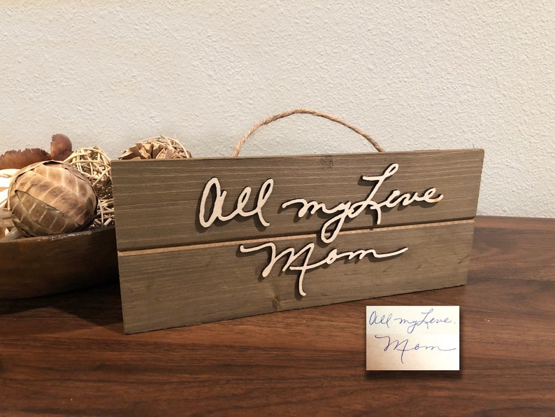 May include: A rustic wooden sign with the words "All my love Mom" written in cursive on it. The sign is hanging from a piece of twine.