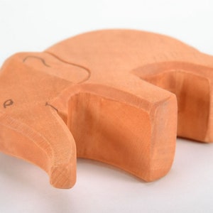May include: A wooden elephant toy, carved from light brown wood. The elephant is lying on its side with its trunk curled up.