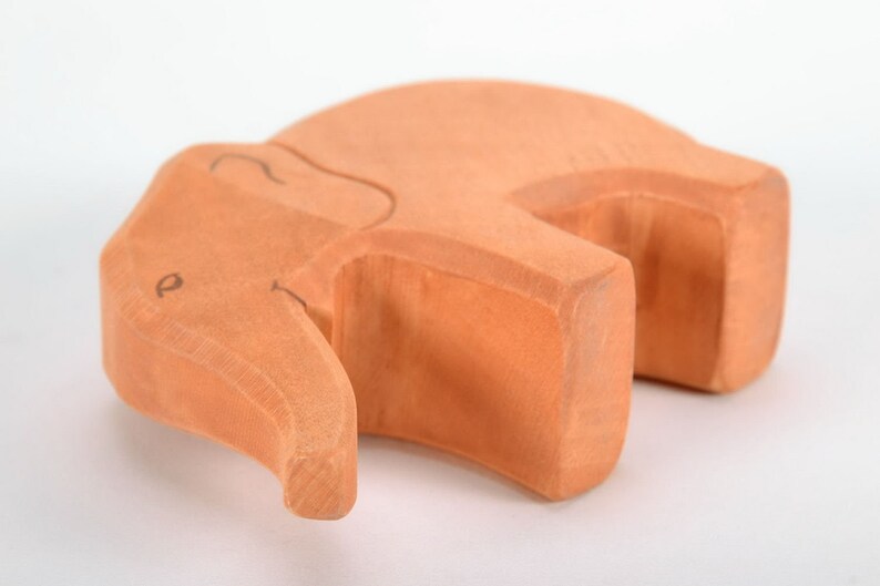 May include: A wooden elephant toy, carved from light brown wood. The elephant is lying on its side with its trunk curled up.