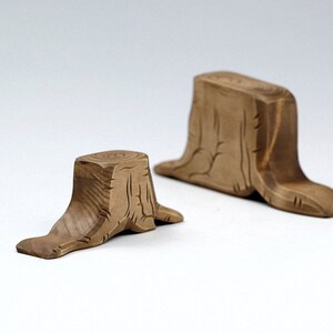 May include: Two wooden tree stump shaped decorative objects. The larger stump is brown and has a more detailed texture. The smaller stump is a lighter brown and has a simpler texture.