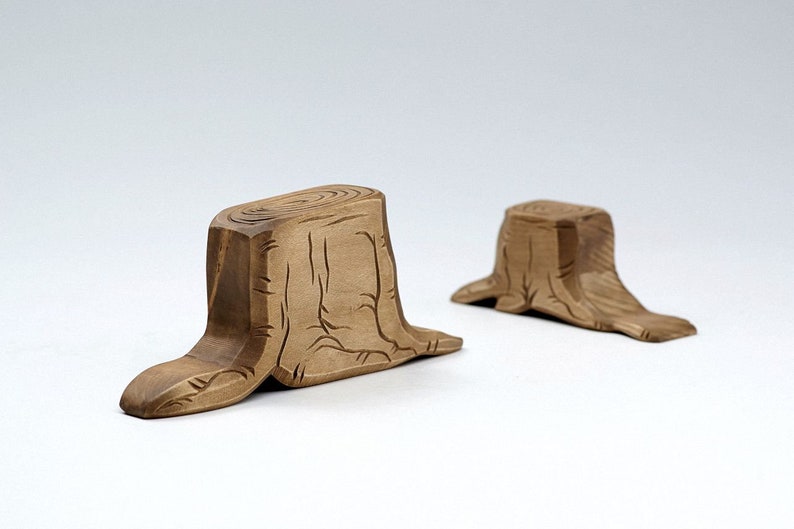 Peut inclure: Deux objets d&eacute;coratifs en bois en forme de souche d'arbre. Les souches sont brunes et pr&eacute;sentent un motif de grain de bois sculpt&eacute;. Les souches sont pos&eacute;es sur une surface blanche.