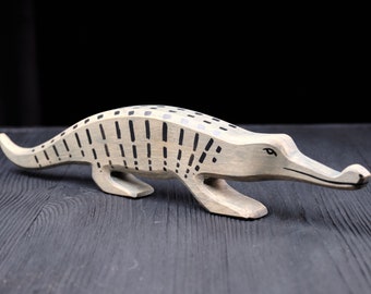 May include: A wooden alligator figurine painted in a light gray color with black stripes. The alligator is posed in a walking position with its head raised and its mouth closed.