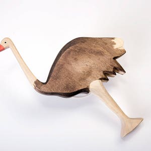 May include: A wooden ostrich toy with a brown body and a light brown neck and legs. The ostrich has a red beak and a white patch on its head.