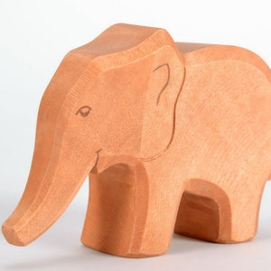 May include: A wooden elephant toy with a light brown finish. The elephant has a long trunk, large ears, and a simple, carved face.