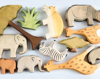 May include: Wooden animal toys including a giraffe, zebra, elephant, rhino, and hippo. The set also includes trees and grass. The toys are made of natural wood and painted in various colors, creating a safari theme.