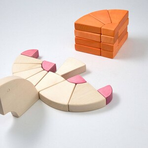 May include: A set of wooden blocks in pink and orange shades. The blocks are shaped like segments of a circle and can be used to build a variety of structures.