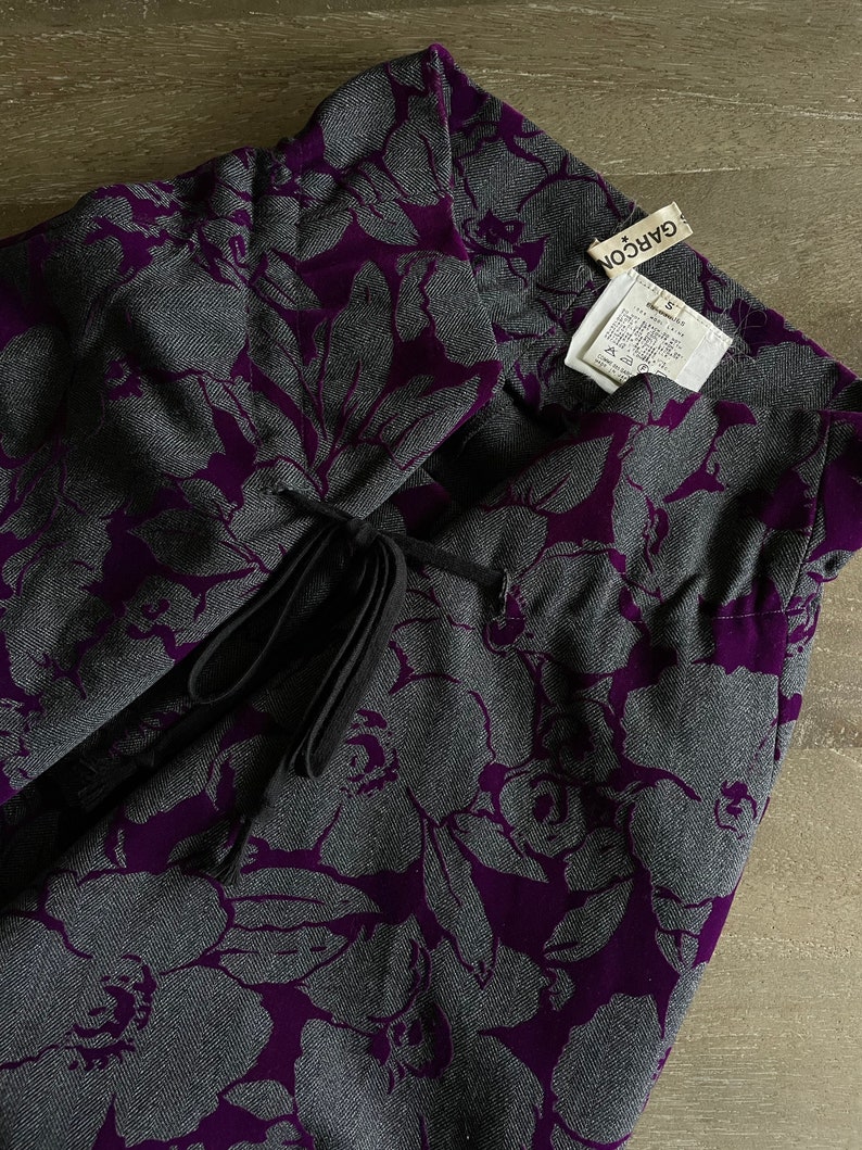 May include: Purple and gray floral skirt with a black drawstring tie. The skirt has a label that reads "GAR&Ccedil;ON" and "S".
