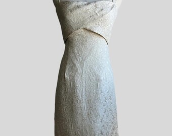 May include: A white sleeveless dress with a brocade pattern. The dress has a fitted bodice and a skirt that falls to the knee.